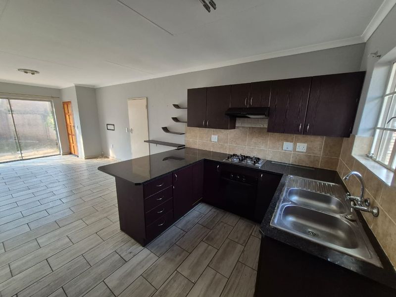 Open-plan kitchen and living area featuring dark wood cabinetry, granite countertops, gas hob, and tiled flooring, leading to an outdoor patio area.