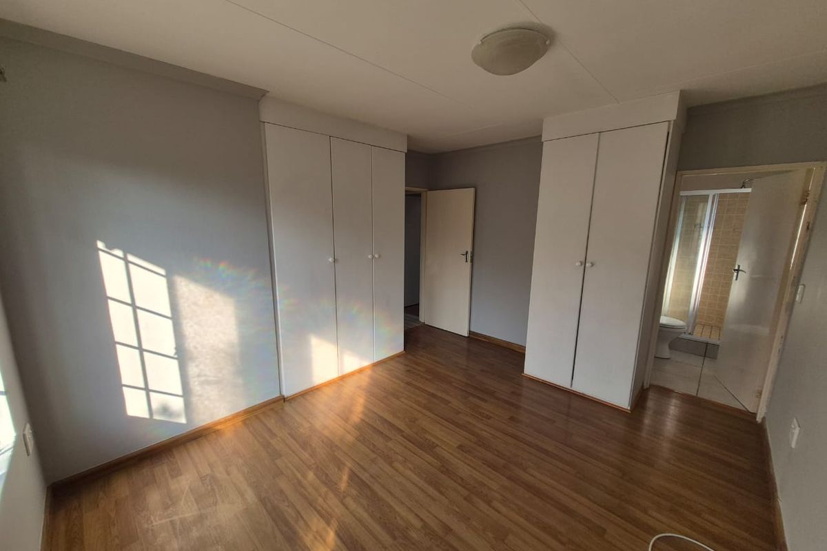 A bright, empty bedroom featuring laminate flooring, built-in cupboards, and direct access to an en-suite bathroom.