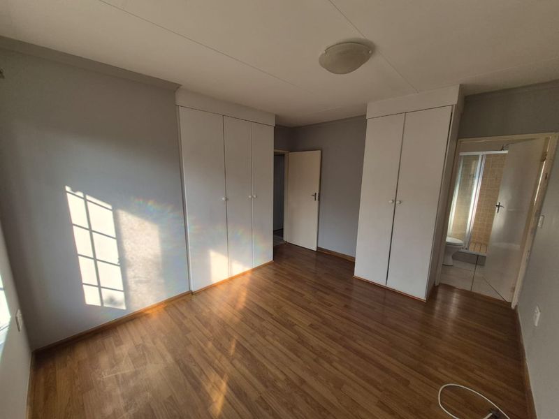 A bright, empty bedroom featuring laminate flooring, built-in cupboards, and direct access to an en-suite bathroom.