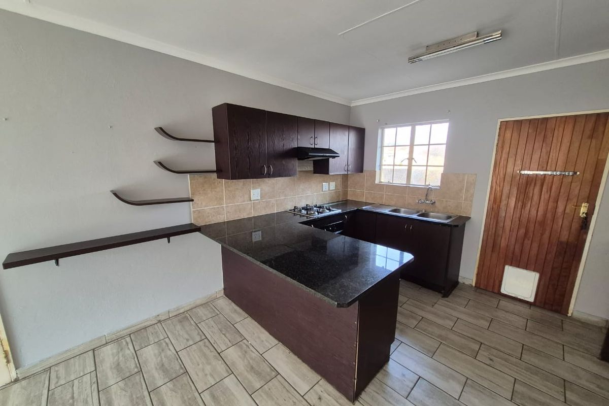 A functional kitchen featuring dark cabinetry, granite countertops, a gas hob with extractor, and tiled flooring, offering a clean and practical workspace.