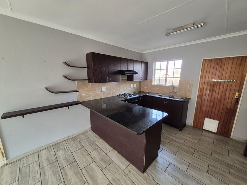 A functional kitchen featuring dark cabinetry, granite countertops, a gas hob with extractor, and tiled flooring, offering a clean and practical workspace.