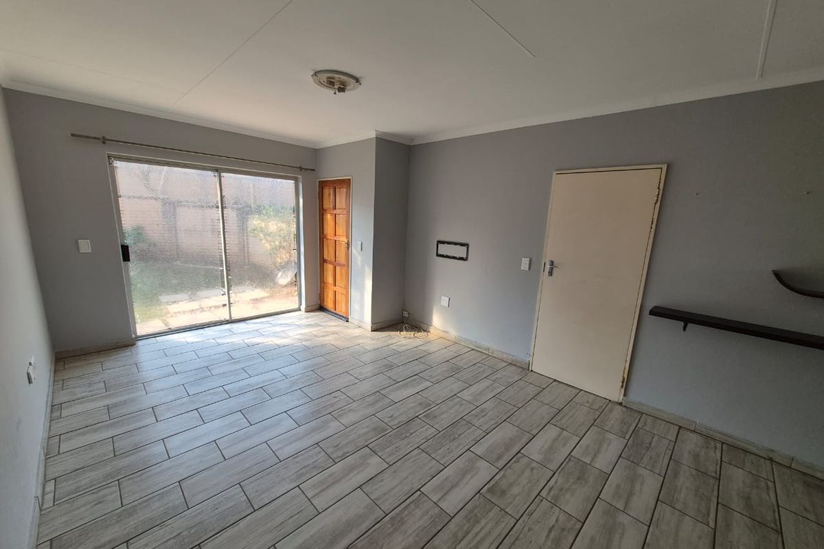 An empty living room featuring tiled flooring, a sliding glass door leading to the exterior, and neutral grey walls.