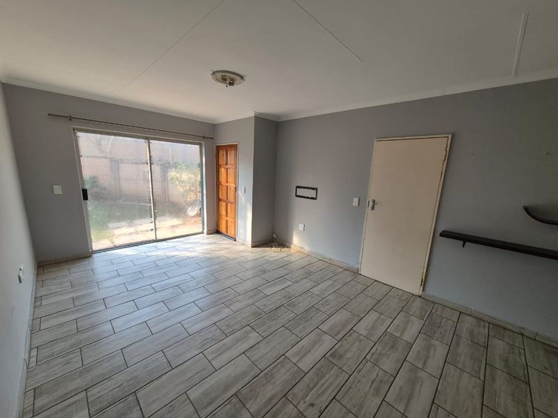 An empty living room featuring tiled flooring, a sliding glass door leading to the exterior, and neutral grey walls.