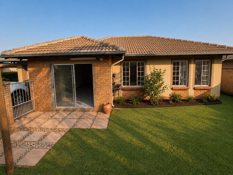 Rear view of the townhouse featuring a brick facade, tiled roof, paved patio area, and a well-maintained lawn.