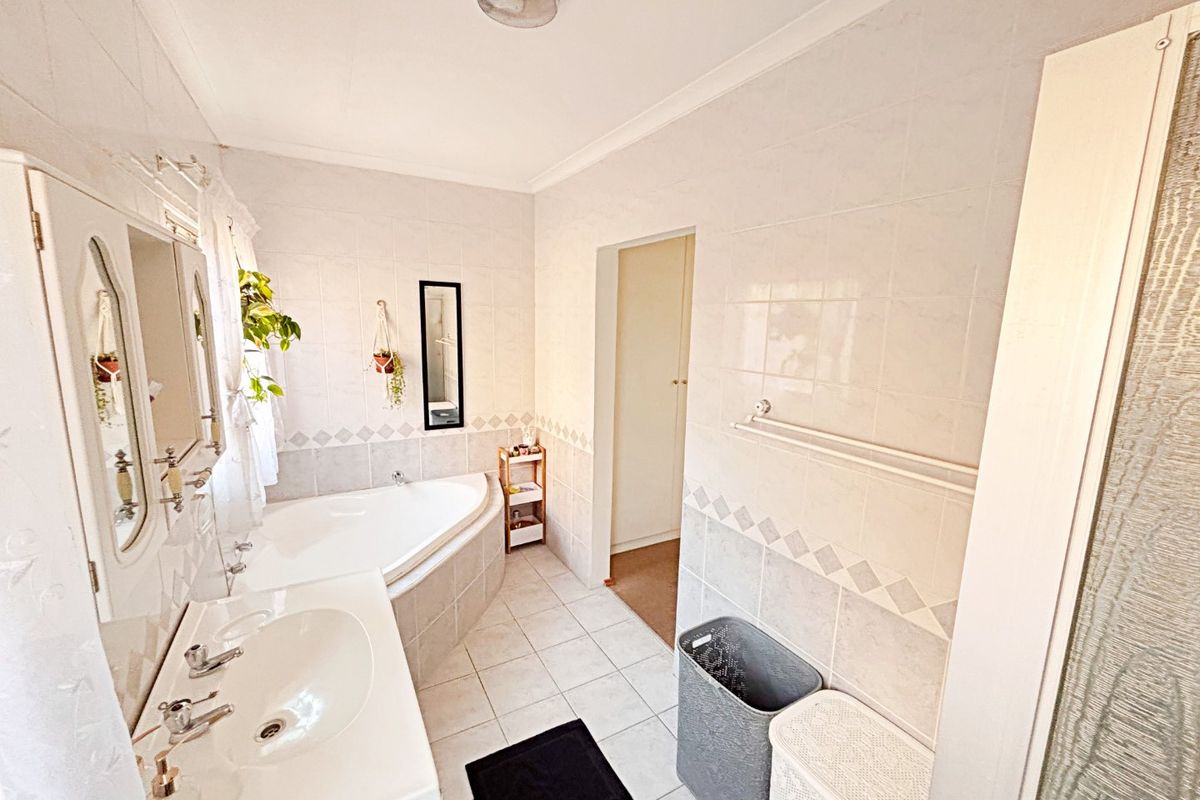 A functional bathroom featuring a corner bathtub, pedestal washbasin, and neutral ceramic tiling throughout.
