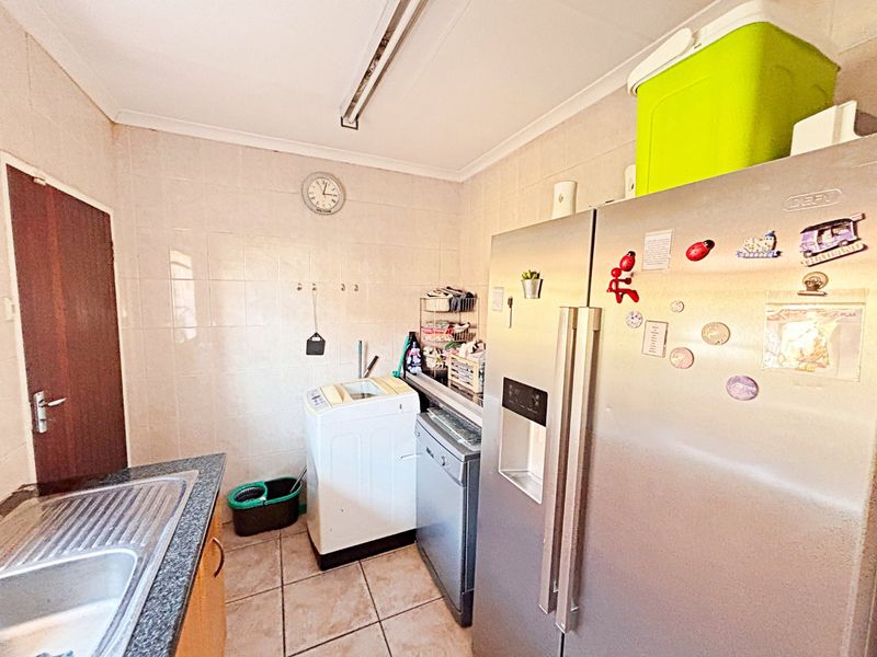A functional laundry area featuring tiled walls, tiled flooring, a stainless steel sink with granite countertop, and space for laundry appliances.