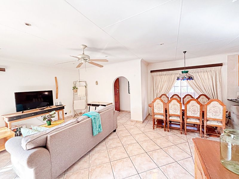 Spacious open-plan living and dining area featuring tiled flooring, a ceiling fan, and a classic arched doorway leading to other parts of the home.