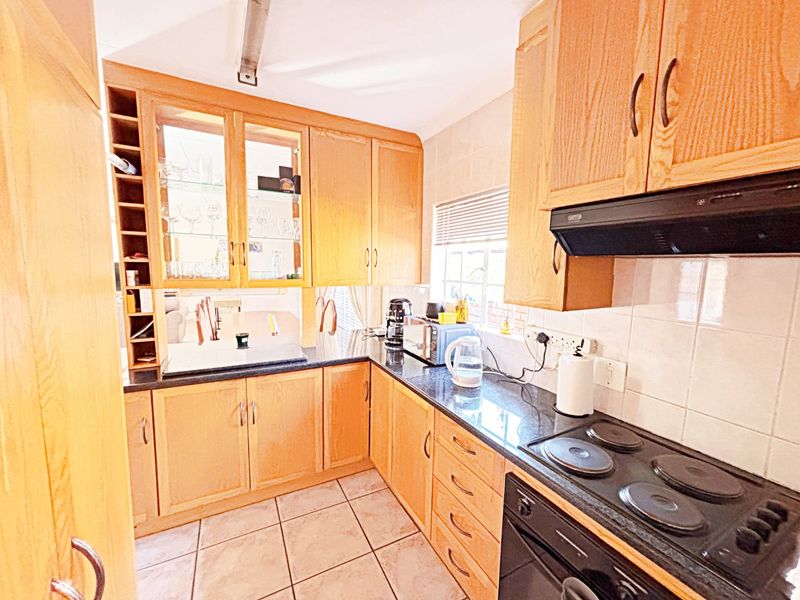 A functional kitchen featuring wooden cabinetry, granite countertops, an electric hob, and built-in oven with tiled flooring and backsplash.