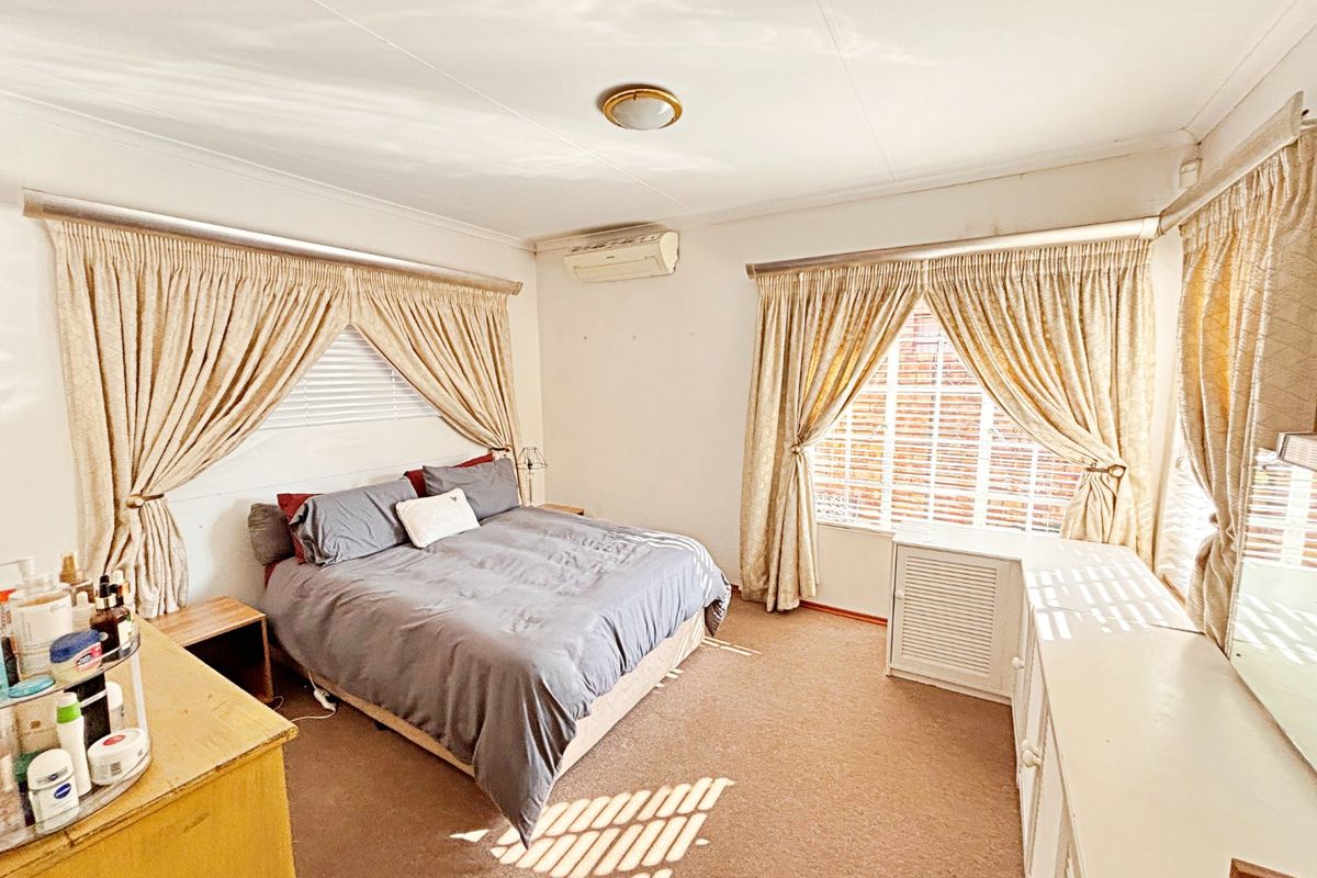 A spacious bedroom featuring carpeted flooring, an integrated air conditioning unit, and large windows with curtain rails.