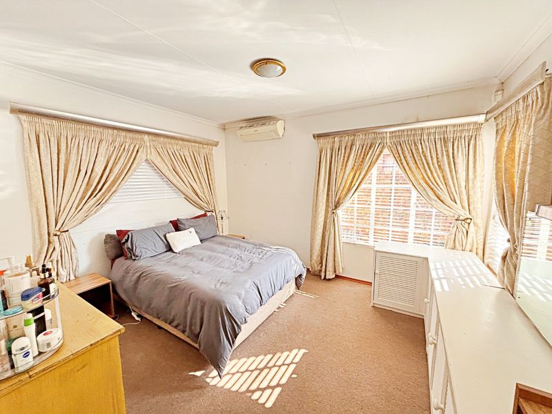 A spacious bedroom featuring carpeted flooring, an integrated air conditioning unit, and large windows with curtain rails.