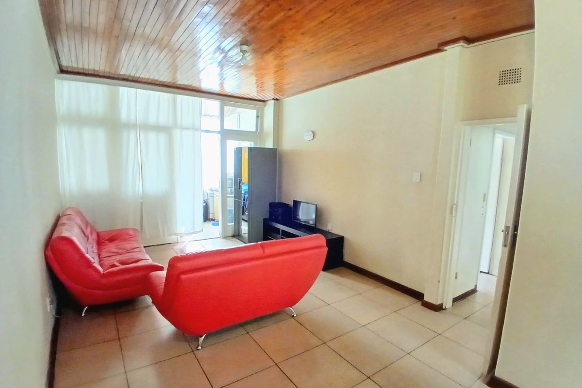 A living room featuring tiled flooring and a timber tongue and groove ceiling, with access to an adjoining balcony through a sliding glass door.
