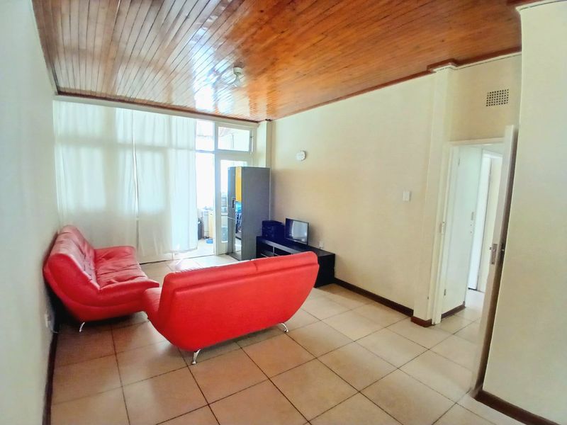 A living room featuring tiled flooring and a timber tongue and groove ceiling, with access to an adjoining balcony through a sliding glass door.