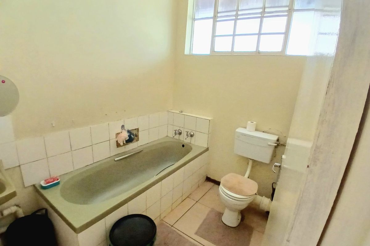 A dated bathroom featuring a built-in bathtub with tiled splashback, a standard toilet, and a high-set window providing natural light.