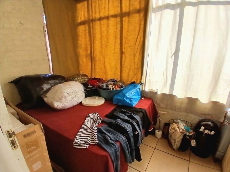 A compact bedroom featuring tiled flooring and a large window, currently used for storage.