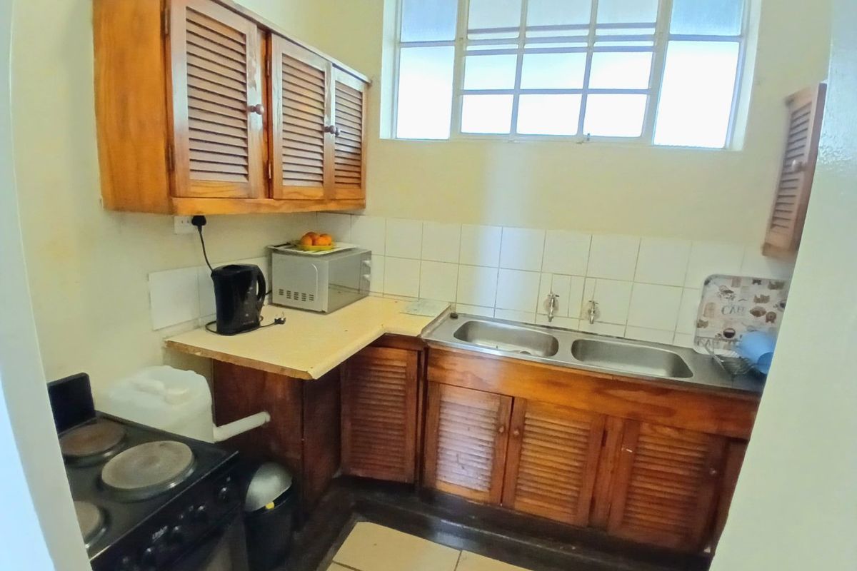 A compact kitchen featuring dated louvered timber cabinetry, a double bowl stainless steel sink, tiled splashback, and ceramic floor tiles.