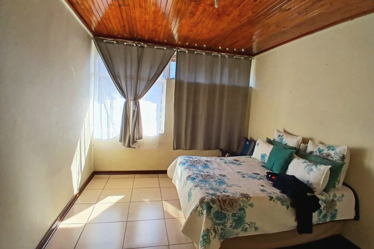 A bedroom featuring tiled flooring and a wooden tongue and groove ceiling, offering a functional space with potential for cosmetic updates.
