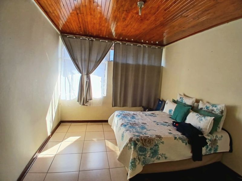 A bedroom featuring tiled flooring and a wooden tongue and groove ceiling, offering a functional space with potential for cosmetic updates.