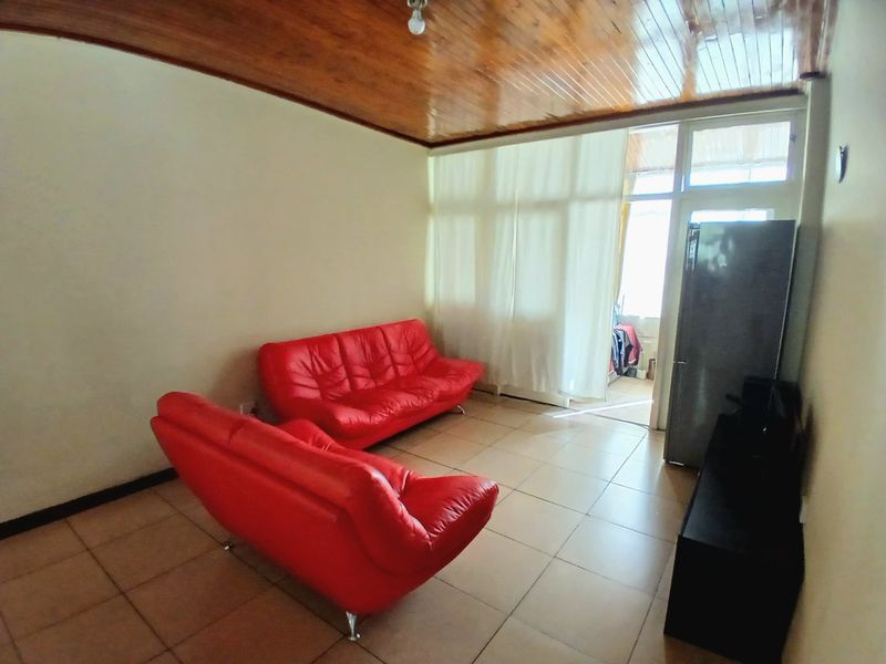 A living room featuring tiled floors and a timber-paneled ceiling, with direct access to an adjoining balcony area through a glass sliding door.