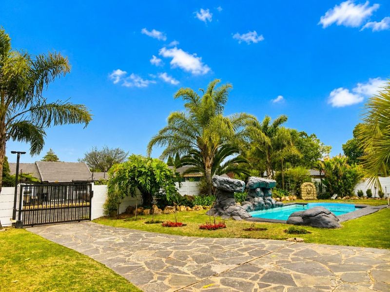 A well-maintained outdoor pool area featuring a decorative rock feature, stone paving, and a secure gated entrance within a landscaped garden setting.