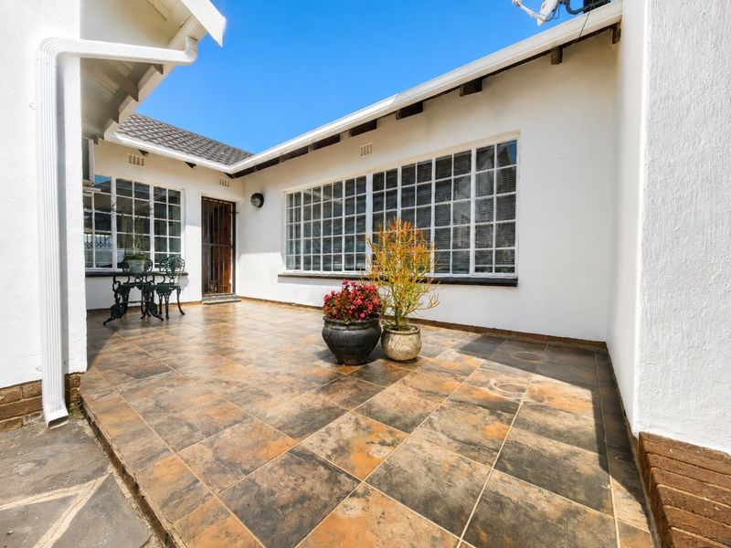 A spacious outdoor patio area featuring tiled flooring, exposed rafters, and large multi-pane windows, providing a functional space for outdoor living.