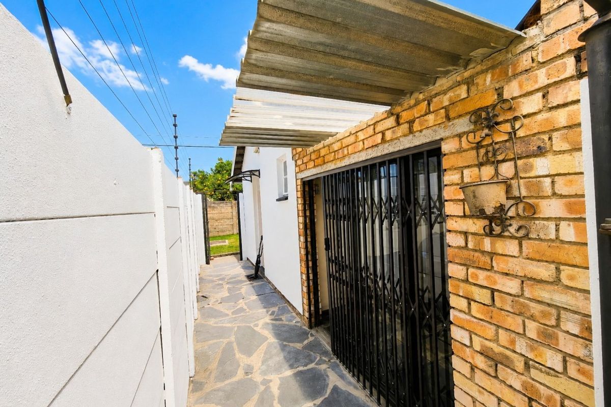 A narrow side passage featuring stone paving, a brick wall with a security gate, and a corrugated roof covering.