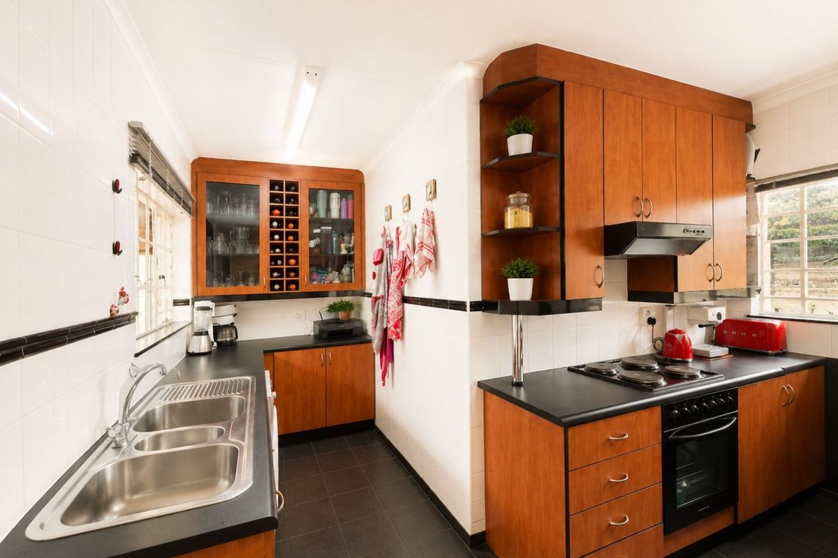 A functional kitchen featuring warm-toned wooden cabinetry, dark laminate countertops, a double stainless steel sink, and integrated cooking appliances with tiled finishes.