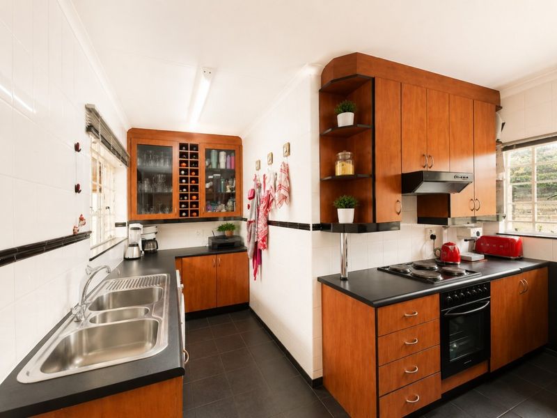 A functional kitchen featuring warm-toned wooden cabinetry, dark laminate countertops, a double stainless steel sink, and integrated cooking appliances with tiled finishes.