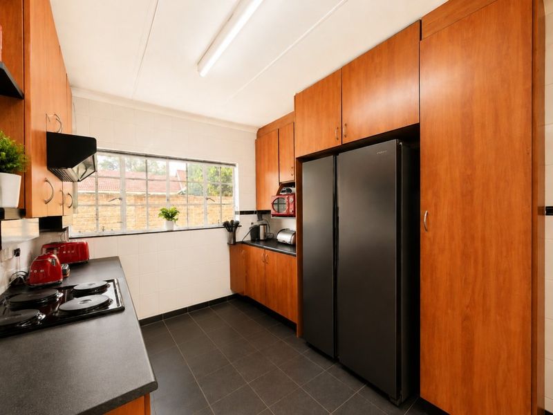 A functional kitchen featuring wood-finish cabinetry, dark countertops, an electric hob with extractor fan, and tiled flooring with a window overlooking the rear exterior.