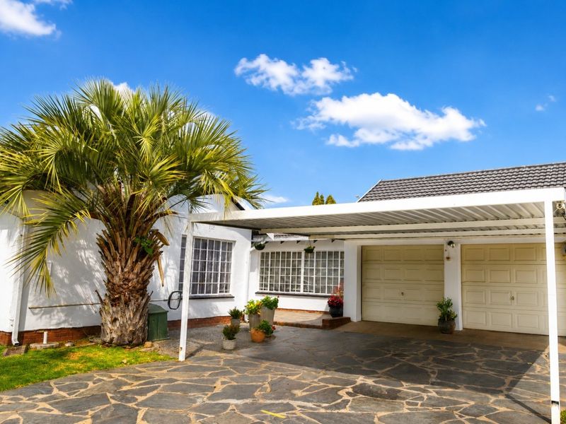 Front exterior view featuring a double garage, covered carport, and paved driveway area with established landscaping.