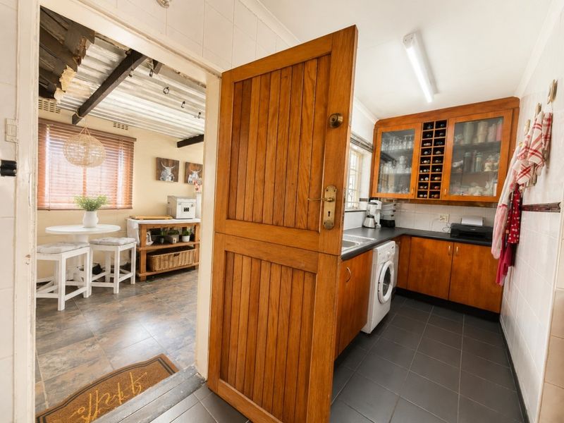 A functional scullery featuring wooden cabinetry, built-in wine storage, tiled backsplash, and direct access to an adjacent living area.