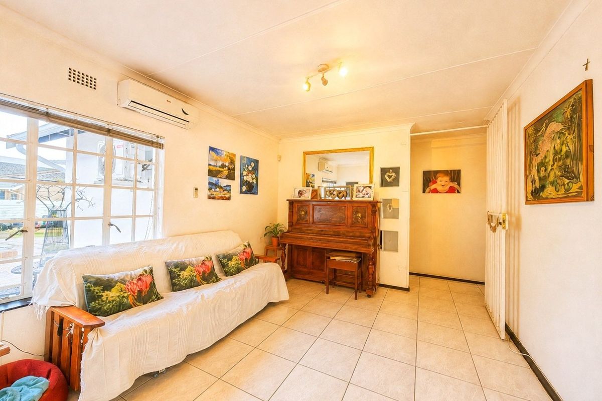 A bright living room featuring tiled flooring, a wall-mounted air conditioning unit, and a security gate, offering a functional and well-lit living space.