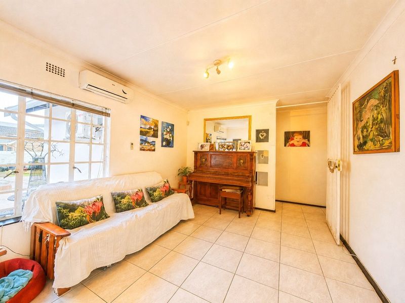 A bright living room featuring tiled flooring, a wall-mounted air conditioning unit, and a security gate, offering a functional and well-lit living space.