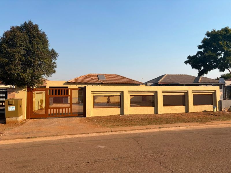Front exterior view of a house featuring a perimeter wall, metal driveway gate, and tiled roof with a solar water heater panel.