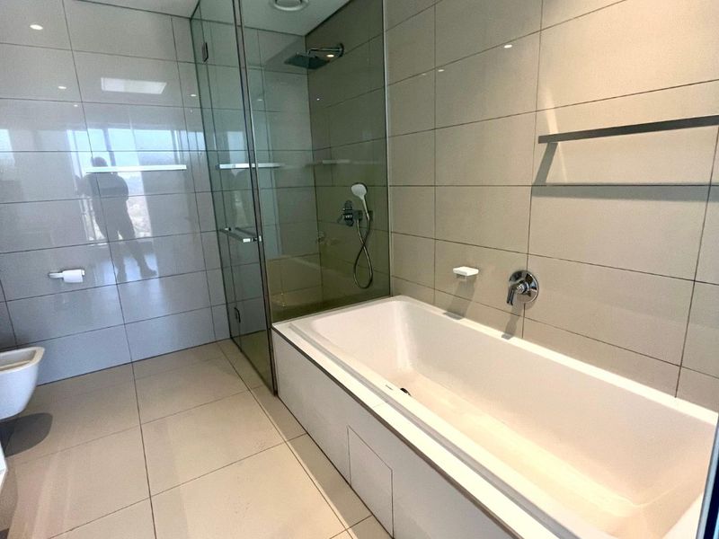 Modern bathroom featuring a built-in bathtub, a separate glass-enclosed shower with rain shower head, and neutral floor-to-ceiling tiling.