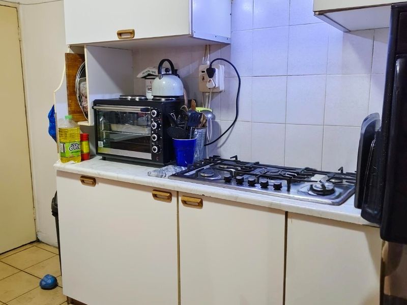 A compact kitchen featuring white cabinetry, a gas hob with an extractor fan, and tiled flooring. The space is functional but dated.