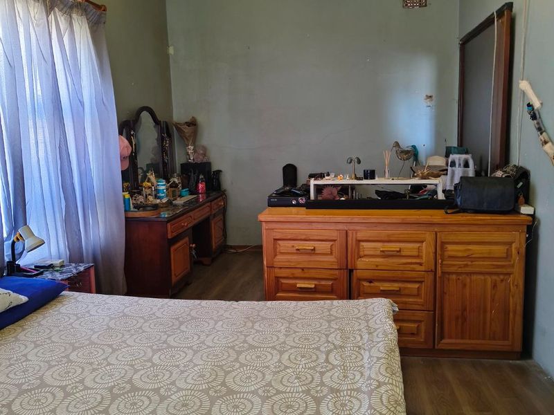 A bedroom featuring laminate flooring and a ceiling-mounted projector, currently showing signs of wear on the wall finishes.