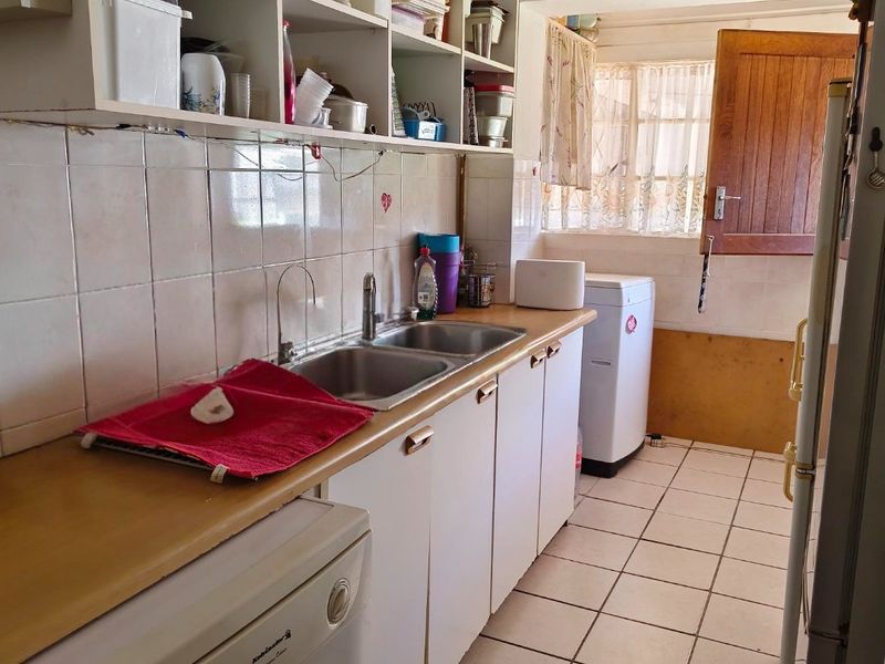 Functional scullery area featuring a double stainless steel sink, laminate countertops, built-in open shelving, and ceramic floor tiles with direct access to the exterior.