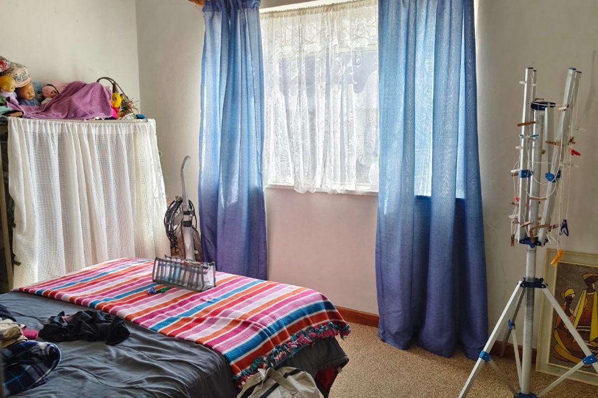A bedroom featuring a window with a curtain rod and ventilation grille, showing signs of wear including visible wall cracks.