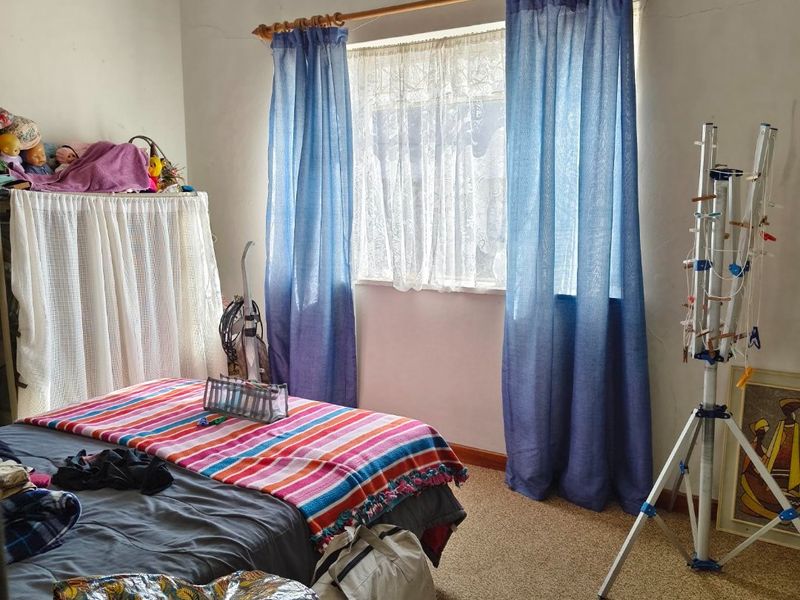 A bedroom featuring a window with a curtain rod and ventilation grille, showing signs of wear including visible wall cracks.