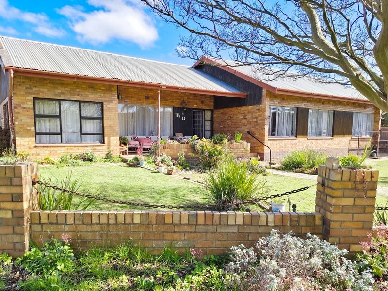 A single-story face brick house featuring a corrugated metal roof, a front porch, and a landscaped garden with a brick boundary wall.