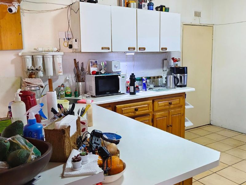 A functional kitchen featuring wooden cabinetry, laminate countertops, and tiled flooring, offering a practical layout with integrated storage and a water filtration system.
