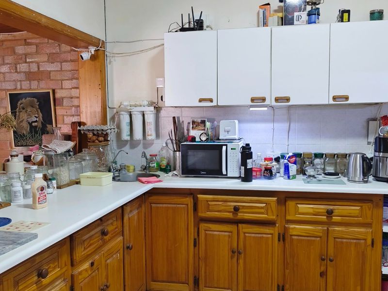 A functional kitchen featuring timber cabinetry, laminate countertops, tiled flooring, and an exposed brick feature wall, requiring cosmetic updates to modernize the space.