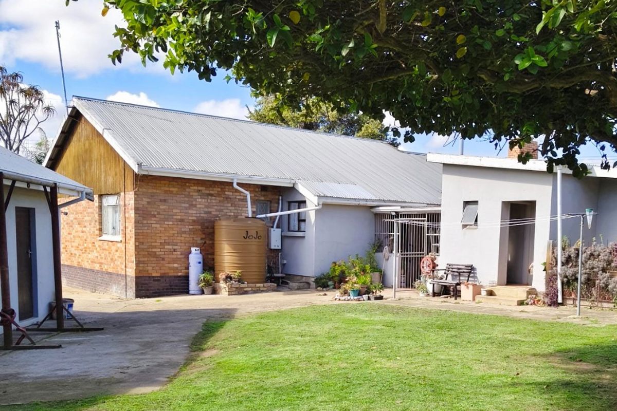Rear view of the property featuring a brick and rendered facade, corrugated metal roof, water storage tank, and a spacious garden area.