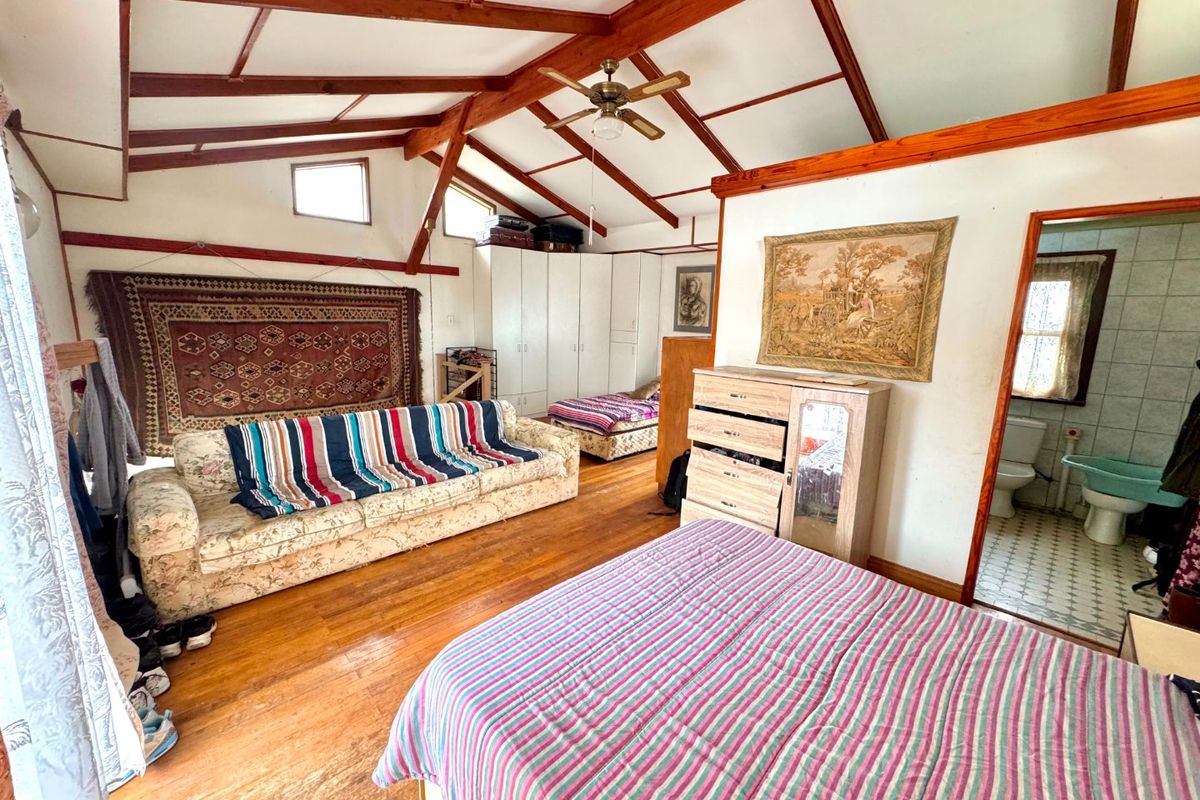 Spacious bedroom featuring exposed timber ceiling beams, hardwood flooring, and built-in storage, with an adjoining en-suite bathroom.