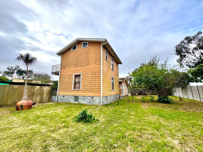 Rear view of a two-story house featuring timber weatherboard cladding, a small balcony, and a large backyard area.