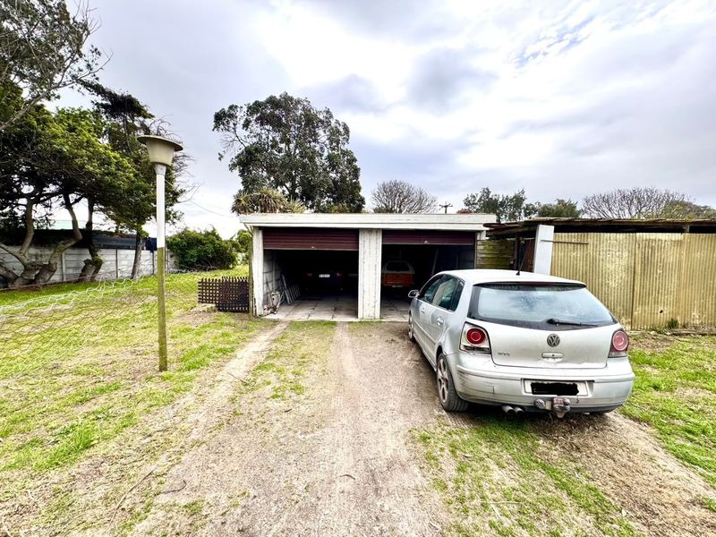 A detached double garage with a concrete driveway and surrounding garden area, showing signs of wear and requiring maintenance.