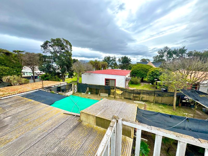 Elevated view of the rear yard showing corrugated roofing, perimeter fencing, and surrounding garden area.