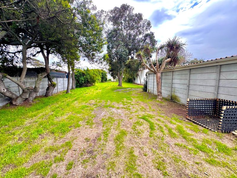 A spacious, level backyard area enclosed by precast concrete boundary walls, featuring mature trees and potential for landscaping development.