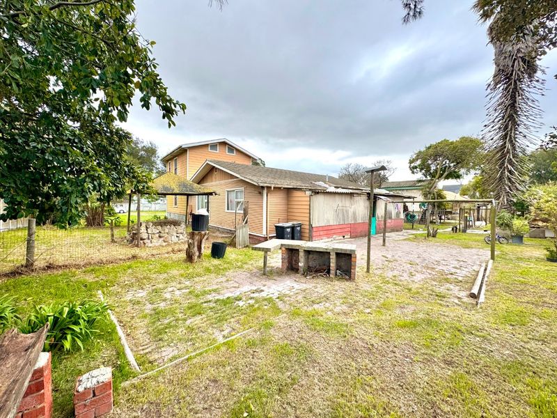 Rear exterior view of the property featuring a paved patio area, brick barbecue, and weatherboard cladding in need of maintenance.