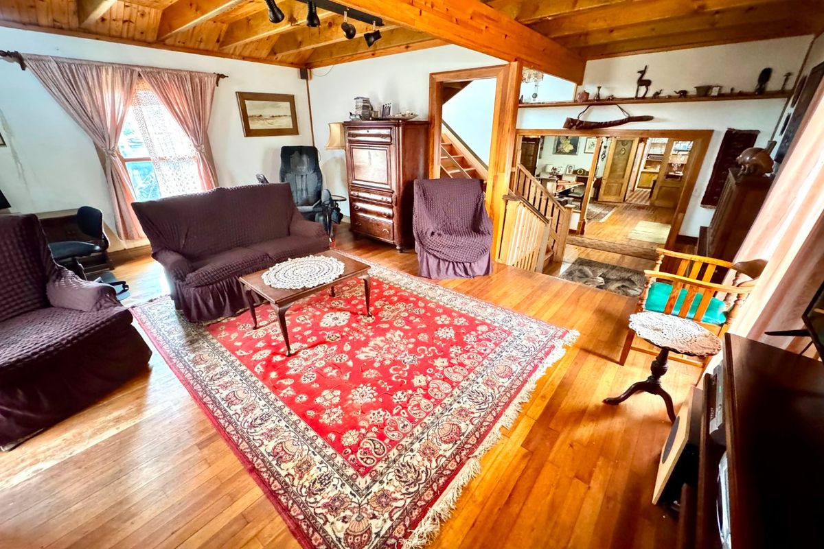 Spacious living area featuring exposed timber ceiling beams, warm hardwood flooring, and an open staircase leading to the upper level.